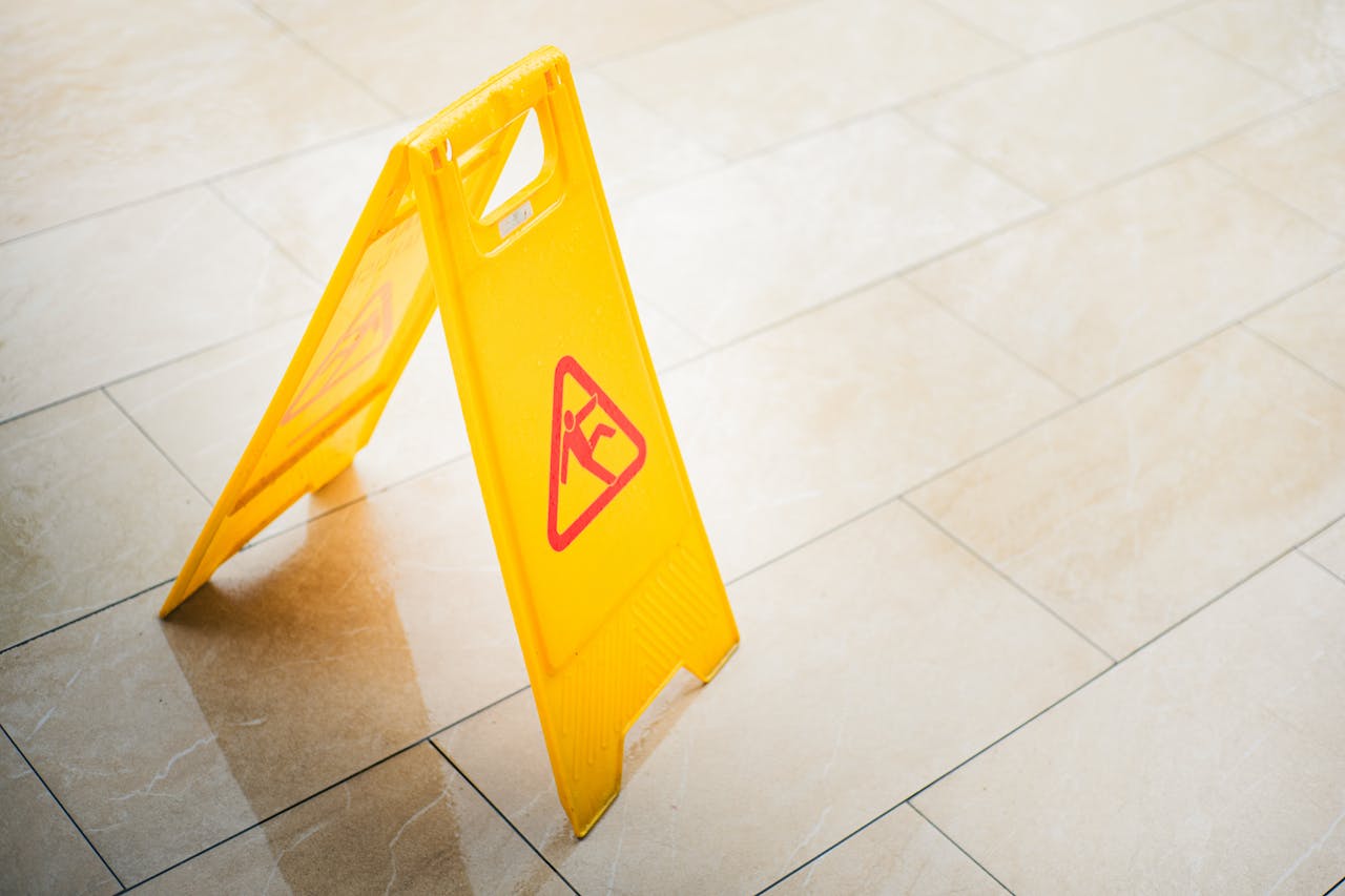 services-03 A bright yellow caution sign on a tiled floor indicates a wet surface, alerting passersby to potential hazards.