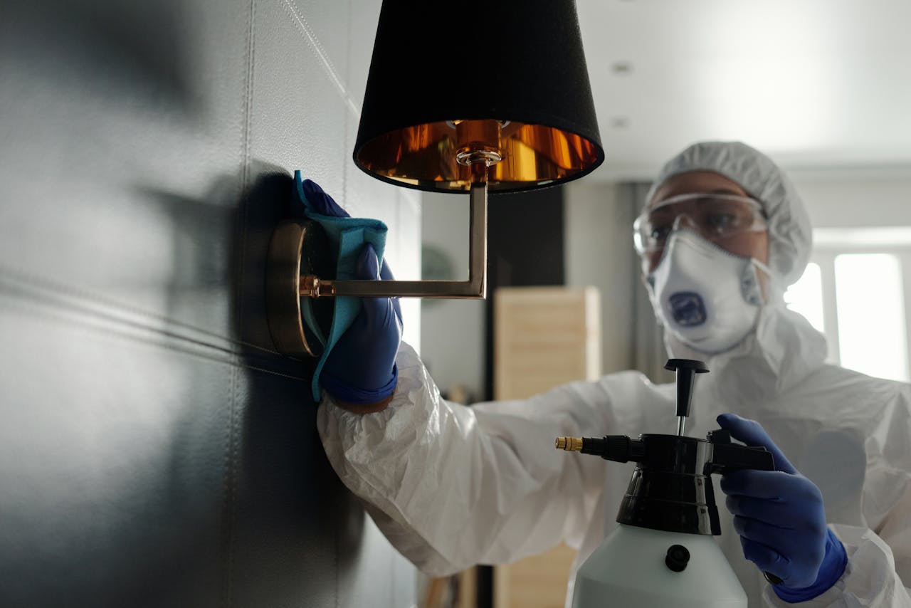 gallery-6 A person wearing protective gear sanitizes a wall lamp to prevent virus spread.