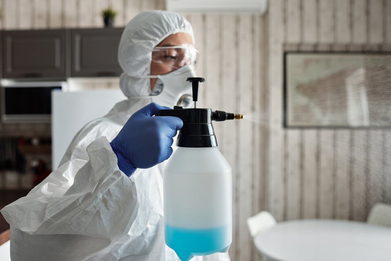 hero-img-01 Professional in full gear disinfecting indoor area using a spray bottle for COVID-19 prevention.