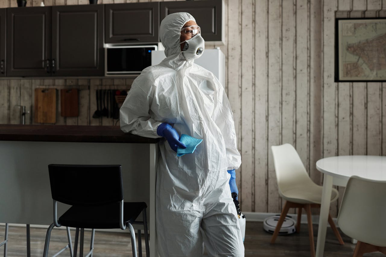 hero-img-02 A person in full PPE gear standing indoors, emphasizing disinfection during COVID-19.